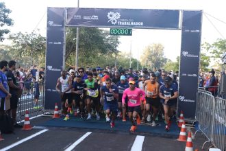 Corredores iniciando prova de rua sob pórtico da Corrida do Trabalhador no Parque do Sabiá, em Uberlândia, com público acompanhando nas laterais